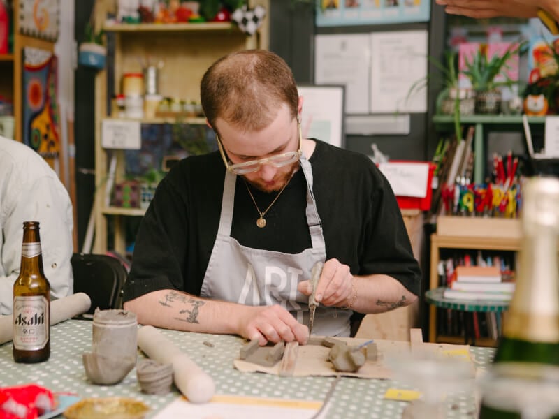 A man sits at a table cutting pottery clay with a sharp instrument